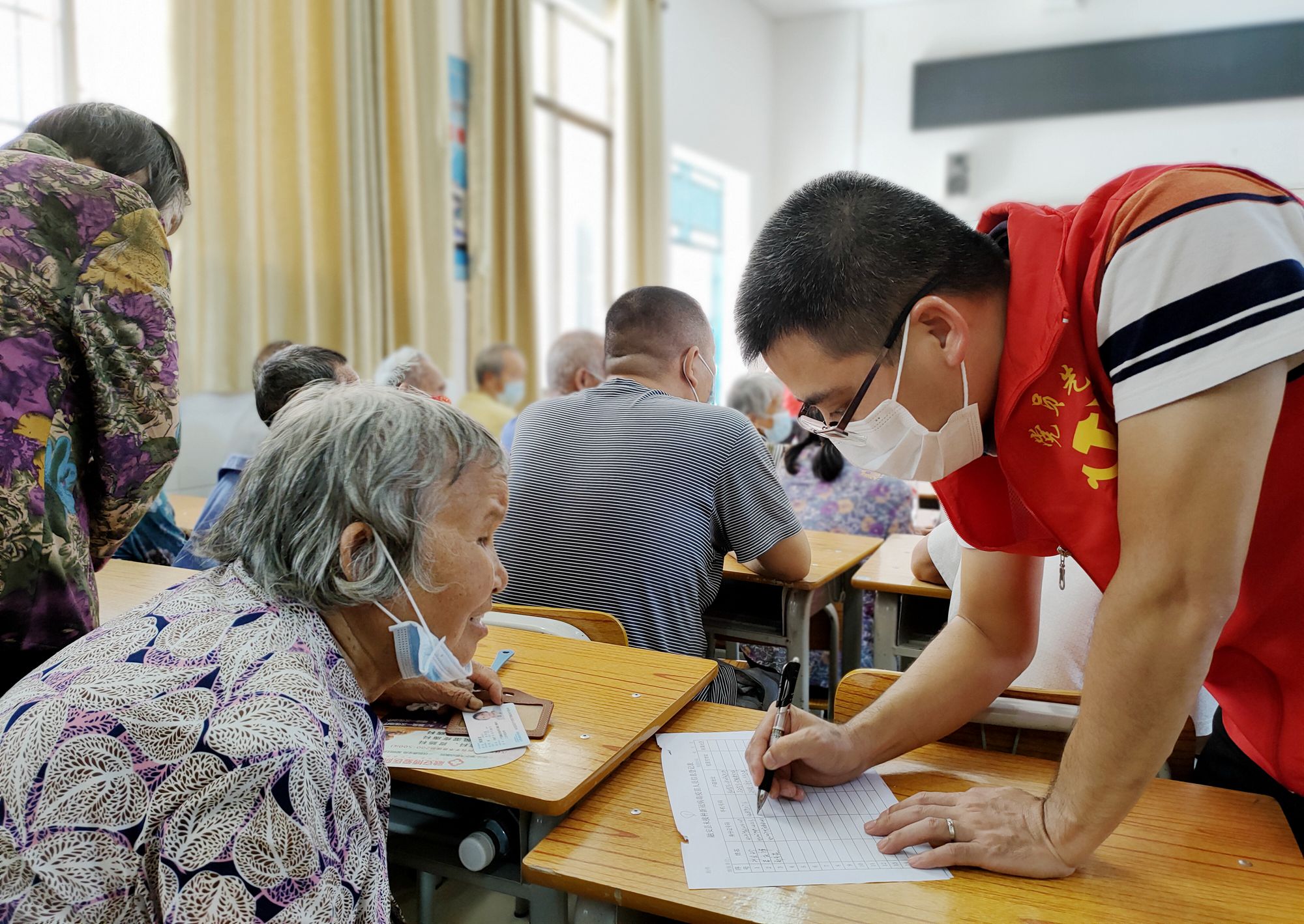 图3:8月19日,在融安县浮石镇东江村疫苗接种点,一名党员干部(右)在帮助群众做接种疫苗登记工作。.jpg